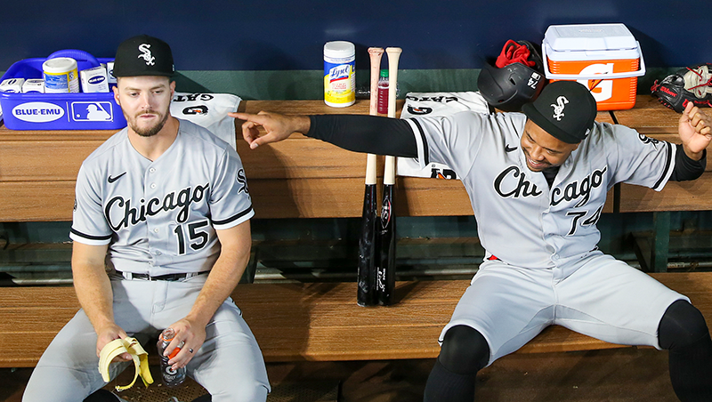 Zack-Collins sitting in the dugout eating a banana and looking completely distraught. Next to him, Eloy-Jimenez is pointing at something off camera and laughing hysterically.