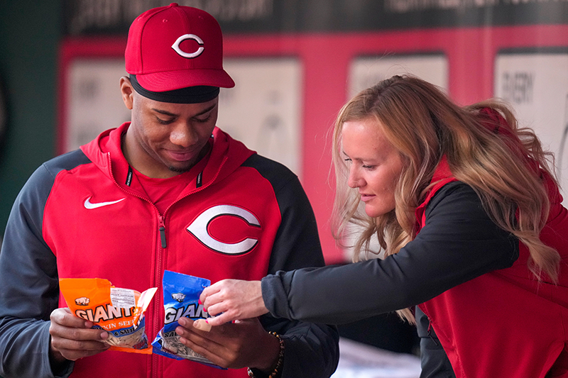 Greene and a blonde woman, both in Reds gear, are in the Royals dugout poring over the backs of two bags of seeds.