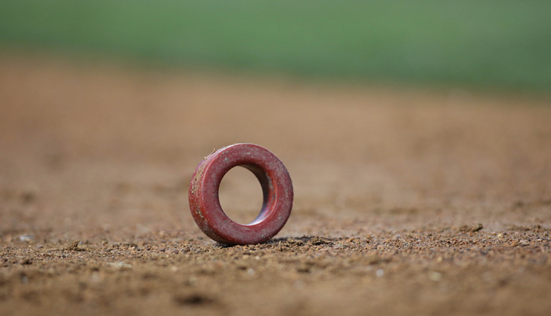 A little red batting doughnut sitting on the dirt.