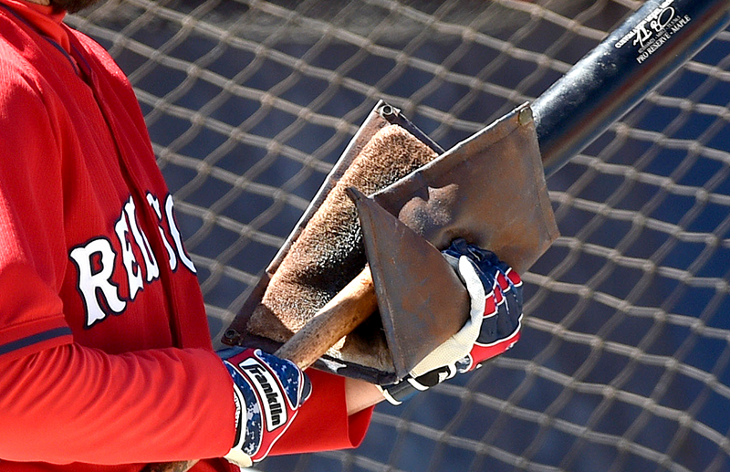 A closeup of a player on the Red Sox applying pine tar to his bat with a pine tar applicator. The inside of the applicator looks like some sort of wool. It's loaded with black pine tar.