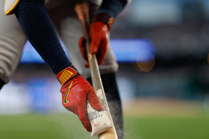 A closeup of a player tapping the trademark of their bat with a rosin bag. A small puff of dust emanates from it.